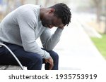 Profile of a sad black man complaining alone sitting on a bench in a park