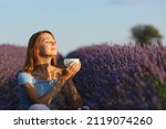 Happy woman relaxing drinking coffee in lavender field at sunset