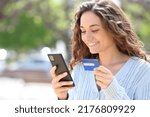 Happy woman buying online with credit card and cell phone in the street
