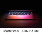 a laptop half closed in the dark with colourful glow
