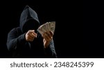Small photo of Portrait bandit man hacker one person wearing hood black shirt, sitting onchair and table thief hand holding money payment counting the amount obtained from hijacking or robbing, in dark background