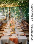 Small photo of outdoor wedding. long banquet tables with white tablecloths , on the tables are flower arrangements, candles, plates with napkins, glasses and cutlery in autumn style