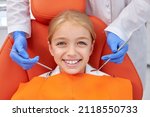 Small photo of Happy caucasian Child girl came to see the dentist. Kid sits in dental chair. Cropped dentist bent over her, top view. Happy patient and dentist concept. Adorable child look at camers smiling