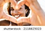 Small photo of Close up image of smiling woman in swimwear on the beach making a heart shape with hands - Pretty joyful hispanic woman laughing at camera outside - Healthy lifestyle, self love and body care concept