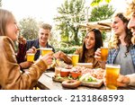 Small photo of Group of multi ethnic friends having backyard dinner party together - Diverse young people sitting at bar table toasting beer glasses in brewery pub garden - Happy hour, lunch break and youth concept