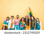 Diverse group of young people celebrating gay pride festival day - Lgbt community concept with guys and girls hugging together outdoors - Multiracial cheerful friends standing on a yellow background 