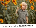 Cute little girl holds sunflower in hand and smiles. Pretty girl of 5 years old wearing green dress is standing in a field of sunflowers. A fun summer walk in a field of sunflowers. Summer holidays