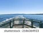 Small photo of View from deck with railing at the stern of a ferry within the Port Townsend Bay with wake of ship and the snowy peaks of the Olympic Mountains of western Washington state, USA in the background