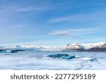 Panoramic view over the frozen glacial lagoon with the terminus or end of the Jokulsarlon glacier, Iceland with in forefront various blue arctic icebergs and snow covered mountain range in background