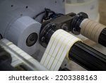 Small photo of A machine for the production of white self-adhesive labels. The shafts of the machine for winding rolls of tape with a label. Die-cutting and cutting of paper for label production. Selective focus