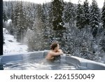 Small photo of Young woman relaxing in a hot tub and thermal spa enjoying a winter view of snowy Christmas trees. Concept of recreation on hot bath and escape to nature