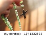 Close up of the holy rosary with hand to pray with light and shadows in dark tone background. Beautiful Roman Catholic item, rosary made from green stone. Life of faith concept. Selective focus. 