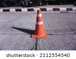 Close-up of traffic cone with white and red stripes on the gray concrete road. Marked border black and white footpath painted road symbol for drivers. Blur background with morning light in Thailand.