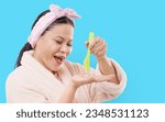 Small photo of Happy cosmetics customer indulges in her skincare routine. An Asian woman in a comfortable bathrobe is shown applying fluent gel onto her hand, highlighting her meticulous approach to personal care