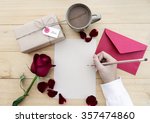 Female hands writing down on letter paper for Valentine's day with gift box and cup of coffee on desk, top view