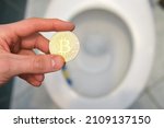 Small photo of man holds bitcoin over the toilet. Concept showing a misguided investment in cryptocurrencies