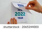 Small photo of Close-up of male hands flipping through the December page of 2021 wall calendar followed by the title page of a new 2022 calendar