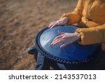 Small photo of Female hands playing a tongue drum musical instrument (metal drum with cut steel tongues and a unique sound). It is very similar to the musical instrument called a handpan, hang or pantam.