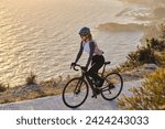 Small photo of Professional female cyclist in cycling clothes riding during a sunset. Bicycle training outdoors. Effortful cycling mood. Cycle in beautiful nature. Woman cyclist wearing cycling kit and helmet. Spain