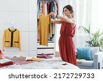 Elegant woman in her bedroom, she is decluttering her wardrobe and choosing clothes