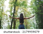 Woman exercising in the forest, she is standing with open arms, back view