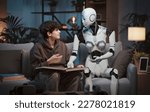 Small photo of AI robot tutor helping a student with homework, they are sitting on the couch at home and reading a book, human-robot interaction concept