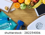 Fitness and weight loss concept, dumbbells, white scale, towels, fruit, tape measure and digital tablet on a wooden table, top view