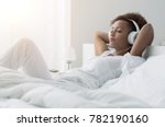 Young beautiful african american woman relaxing and listening to music using headphones, she is lying in bed