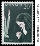 Small photo of TURIN, ITALY - APRIL 29, 2020: A stamp printed in MONACO showing image of nun Bernadette and celebrating the 100th anniversary of the Marian apparition in Lourdes, circa 1958