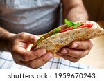 Small photo of Piadina Romagnola with mozzarella cheese, tomatoes, ham and rocket salad in a man's hands. Italian flatbread or open sandwich. Selective focus.