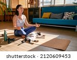 Small photo of Woman practicing yoga and meditation at home sitting on yoga mat in lotus pose with her cat, stretching muscles of legs. Mindful meditation concept. Wellbeing.