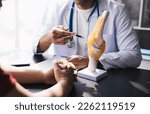 Small photo of Physiotherapist explain an anatomical human knee-joint to an elderly patient. Concept physio treatment and kinesiotherapy.