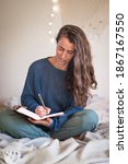 Small photo of Woman in blue sweater writing in leatherbound journal whilst sat on her bed