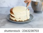 Small photo of Cream cheese icing being spread on a three tier baked hummingbird cake