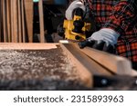 Carpenter craftsman using electric hand wood planer making pool cue or snooker cue in carpentry workplace in an old wooden shed. Handmade craftsman concept. Selective focus on wood planing.