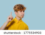 Small photo of seriously boy pointing fingers up, at copy space, isolated over blue background, teenager cu coafura la moda, handsome guy in camasa galbena, tip tanar, nice teenager