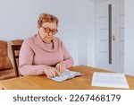 Small photo of An older woman at home, glasses perched on her nose, sits comfortably in her favorite chair, reading a book with rapt attention. Her weathered hands turn the pages with care, lost in the story