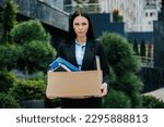 A woman standing outside, holding a box, looking lost and jobless. An unemployed woman with a lost job, holding a box of her belongings. Weight of Loss Woman Carrying Box After Being Fired