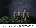 First advent with one burning candle on fir branches with Christmas decoration against a dark grey background, copy space, selected focus, narrow depth of field