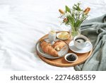 Sunday breakfast in bed with coffee, croissant, jam and boiled egg served on a wooden tray with a bouquet of flowers on mother's day, birthday or valentine's day, copy space, selected focus