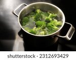 Cooking broccoli in boiling water in a stainless steel pot on the black cooktop in the kitchen, preparation for a healthy vegetable meal, copy space, selected focus, narrow depth of field