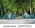 Small photo of Bucharest, Romania - June 17 2023: Two young people sitting on benches in King Mihai I park.