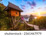 Happy and relaxed travel woman watching sunrise, tree house with diamond beach, Atuh beach in Nusa Penida island, Bali, Indonesia.