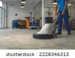 Small photo of Worker polishing hard floor with high speed polishing machine while other cleaner cleans rhe table in the background
