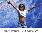 Small photo of In this exuberant moment captured on camera, a jubilant girl celebrates the end of the school year by jumping with unrestrained joy. Wearing heart-shaped pink sunglasses, she gestures energetically, e