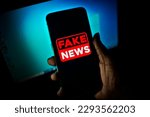 Hand holds a smartphone where the phrase fake news appears on the screen.

Image with news concept and low light