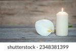 Small photo of WHITE CALLA FLOWER NEXT TO A LIGHTED CANDLE ON WOODEN BACKGROUND. CONDOLENCE CARD. COPY SPACE.