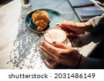 Cappuccino and croissant on the table in the cafe. The morning sunlight falls on the table, beautiful shadows appear. Delicious breakfast.Women's hands hold a cup of coffee.
