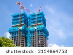 Small photo of Two multistory buildings, the facade is covered with protective construction mesh on a background of a blue sky. Construction of residential buildings, skyscrapers in big city. Construction cranes.