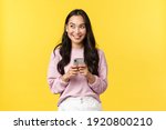 Small photo of People emotions, lifestyle leisure and beauty concept. Dreamy and excited happy young asian woman using mobile phone, smiling and looking upper left corner thoughtful, have idea